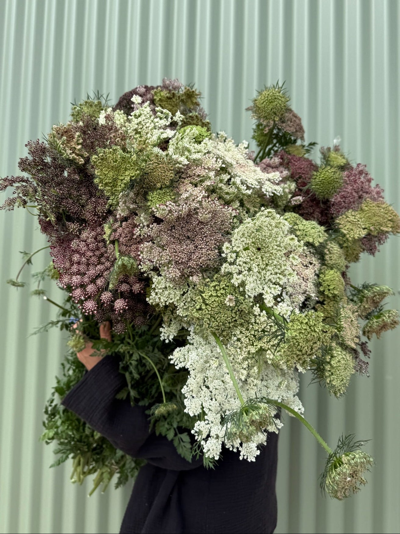 Person holding a large bouquet of flowers against a light green corrugated metal background